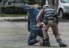 Police officer handcuffing person kneeling on pavement