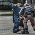 Police officer handcuffing person kneeling on pavement
