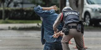 Police officer handcuffing person kneeling on pavement