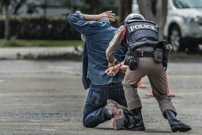 Police officer handcuffing person kneeling on pavement