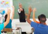 Students raising hands in a classroom while teacher points