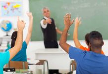 Students raising hands in a classroom while teacher points