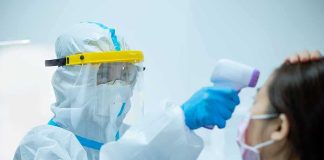 Healthcare worker in PPE checks patient temperature with infrared thermometer
