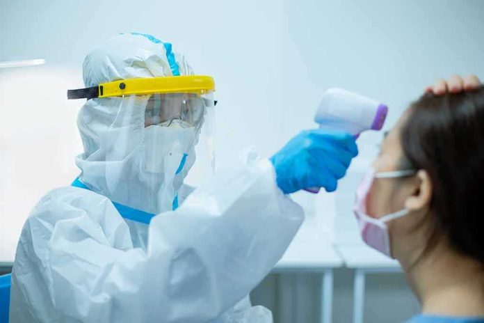 Healthcare worker in PPE checks patient temperature with infrared thermometer