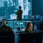 Military analysts monitor data on multiple screens in a command center