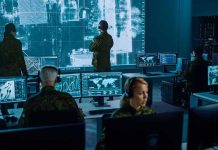 Military analysts monitor data on multiple screens in a command center