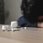 Person with head down near scattered pills on a table