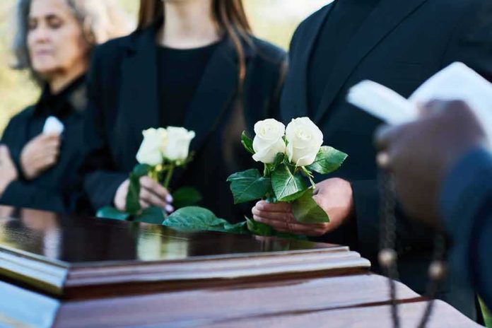 Mourners holding white roses beside a wooden casket
