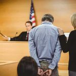 Inside Job Exposed: A Protector Turned Predator Defendant in handcuffs stands before a judge in a courtroom