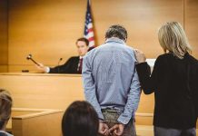 Defendant in handcuffs stands before a judge in a courtroom