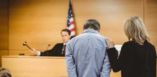 Inside Job Exposed: A Protector Turned Predator Defendant in handcuffs stands before a judge in a courtroom