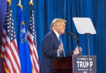 Person speaking at podium with flags in background.