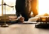 Lawyer writing at desk with scales and gavel