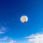 A white balloon floating in a clear blue sky with scattered clouds