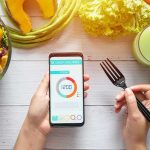 The Truth About the ‘No Dinner After 6’ Rule hands holding phone with calorie tracker beside salad and pastry