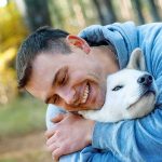 man hugging a white dog outdoors