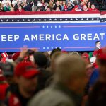 Crowd at political rally in front of large Keep America Great sign