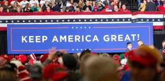 Crowd at political rally in front of large Keep America Great sign