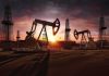 Oil pumpjacks and derricks at sunset in a desert field
