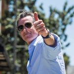 Newsom’s War Chest Skyrockets Amid DOJ Heat man in sunglasses giving a thumbs-up outdoors