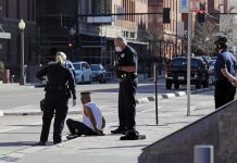 Police officers detain a seated man on a city sidewalk