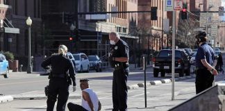 Police officers detain a seated man on a city sidewalk