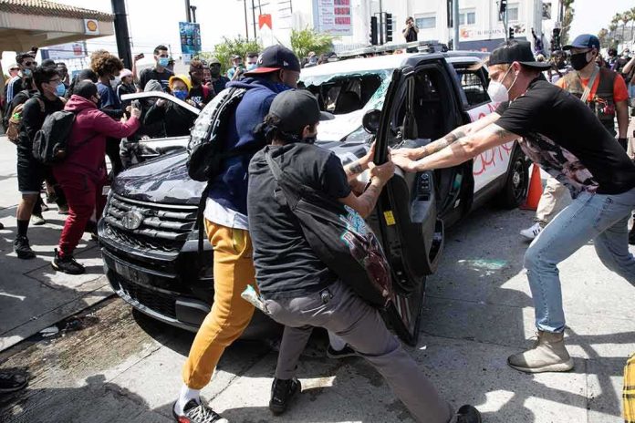 Protesters surround and damage a police vehicle on a city street