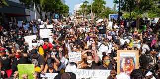 J. C. Tretter, Teddy Williams, and Eugene Sims among protesters kneeling with signs at a large street demonstration
