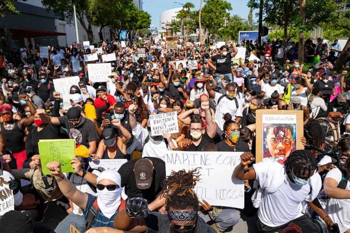 J. C. Tretter, Teddy Williams, and Eugene Sims among protesters kneeling with signs at a large street demonstration