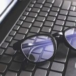 Black eyeglasses resting on a laptop keyboard