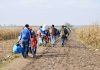 Group of people walking along a muddy farm road with bags and backpacks
