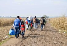 Group of people walking along a muddy farm road with bags and backpacks