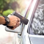 hands holding a handgun aimed near a car window