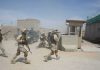 Soldiers in desert uniforms run past a checkpoint amid dust