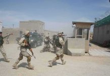 Soldiers in desert uniforms run past a checkpoint amid dust