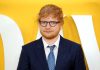 Ed Sheeran in a navy suit against a yellow backdrop