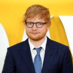 Ed Sheeran in a navy suit against a yellow backdrop