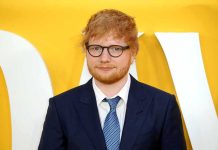 Ed Sheeran in a navy suit against a yellow backdrop