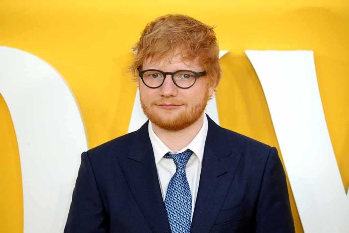 shutterstock_1946174674-1 Ed Sheeran in a navy suit against a yellow backdrop