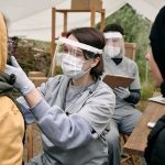 Healthcare worker in PPE examines a patient at an outdoor clinic
