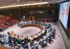 Delegates seated around a circular conference table in a large chamber