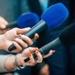 The Hidden Cost of AI Is Hitting Local Communities Reporters holding colorful microphones