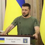From ‘Nazis’ To “Bamboozled” In Kyiv Man at a podium with Ukrainian flags