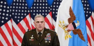 Military officer speaks at podium with U.S. flags behind