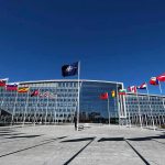 NATO headquarters with member flags in front under a clear blue sky