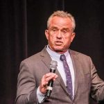 man in a suit speaking into a microphone on stage