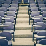 Empty lecture hall with rows of blue seats and foldable desks