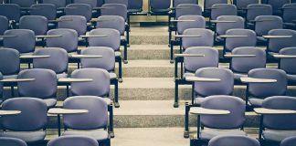 Empty lecture hall with rows of blue seats and foldable desks