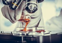 Gloved hand pouring orange liquid into a petri dish under a microscope