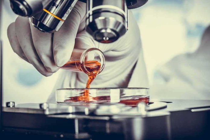 shutterstock_391276264 Gloved hand pouring orange liquid into a petri dish under a microscope